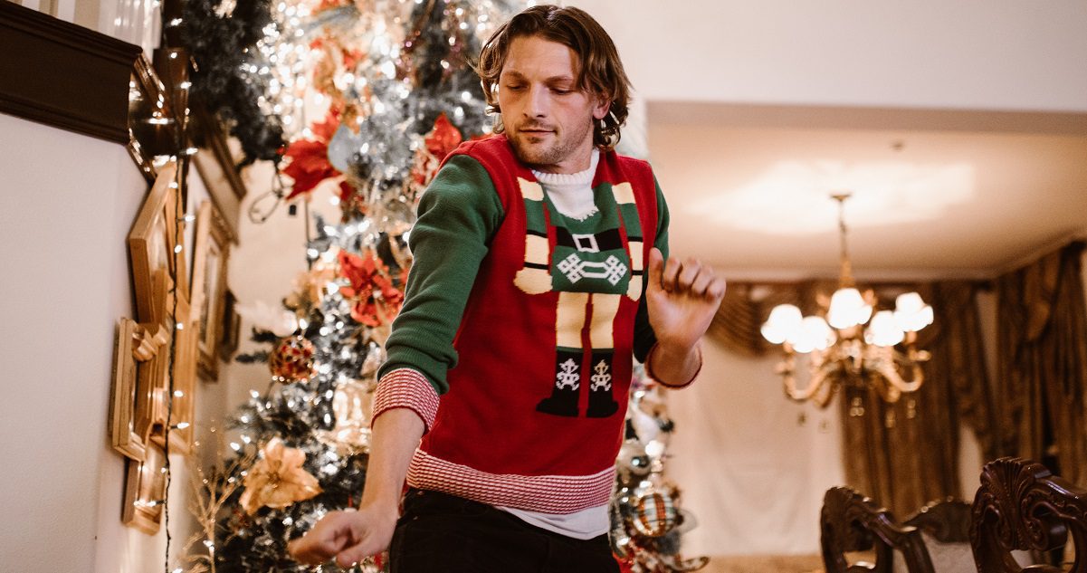 man dressed in a christmas jumper dancing in front of a christmas tree - article for silver magazine www.silver.co.uk