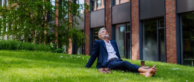 A mature businessman resting and sitting barefoot in park, feeling free, escaping from work, work life balance concept.