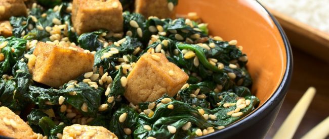 Image shows bowl of asian inspired tofu with spinach and sesame seeds sprinkled on top, with chopsticks resting at the side