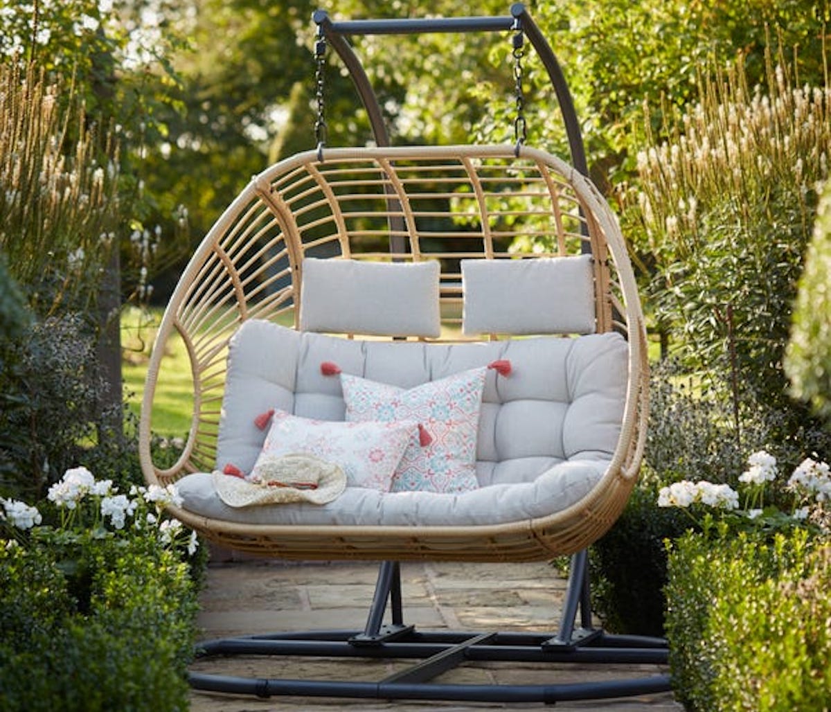 Wicker egg chair hanging in garden with cushions. Best garden party furniture.