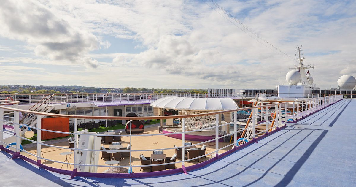 Rooftop of cruise ship. Wicker tables and chairs are spotted on the lower deck near a bar