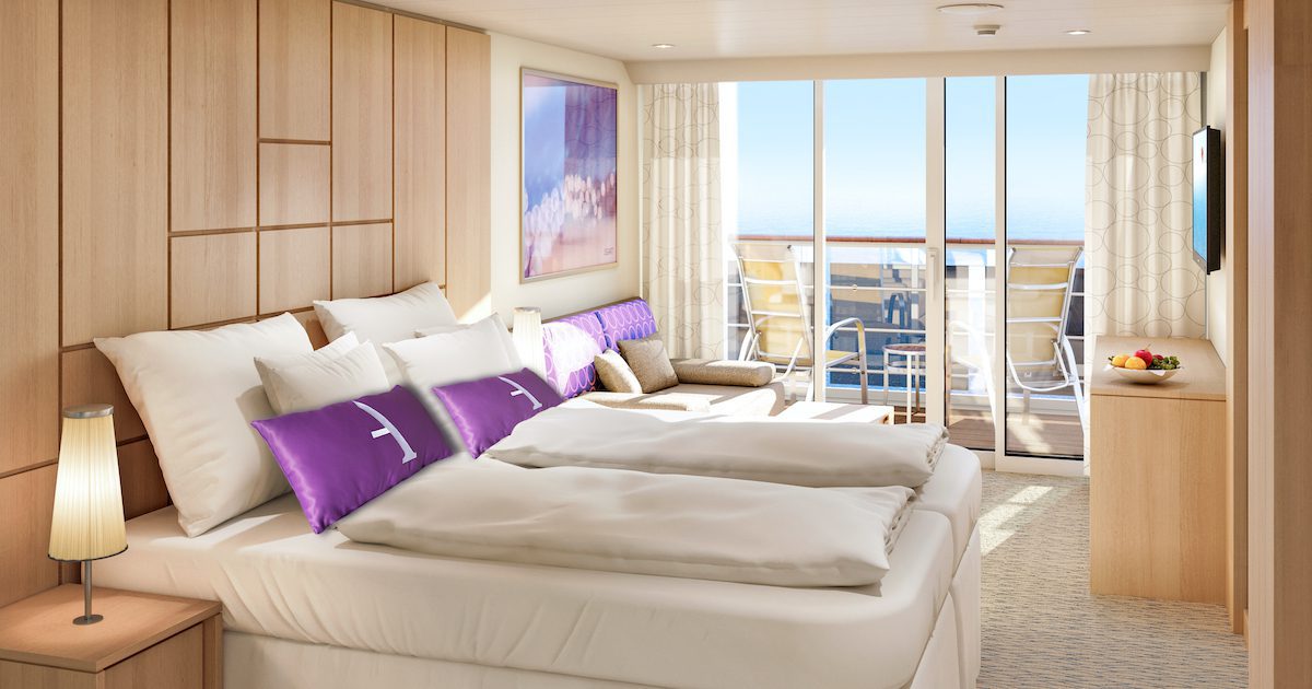 Ambition cruise suite. Wood panelling behind the head of the bed. At the far end of the room a terrace looks out over the blue sky. 