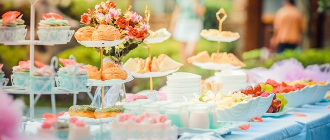 Well decorated cakes displayed on a long table in a back garden. Best garden party tips Silver - www.silvermagazine.co.uk