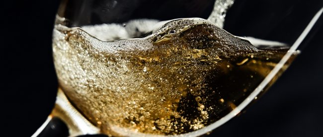 Image shows glass of sparkling wine being poured against a black background