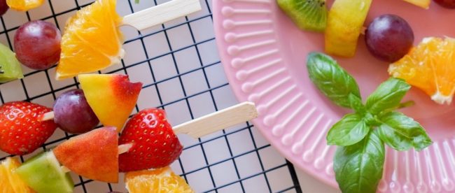 Colourful fruit skewers next to a pink plate. Healthy eating tips on Silver.