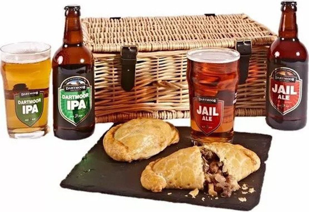 A wicker basket with two bottles of ale, two pasties and two pint glasses.