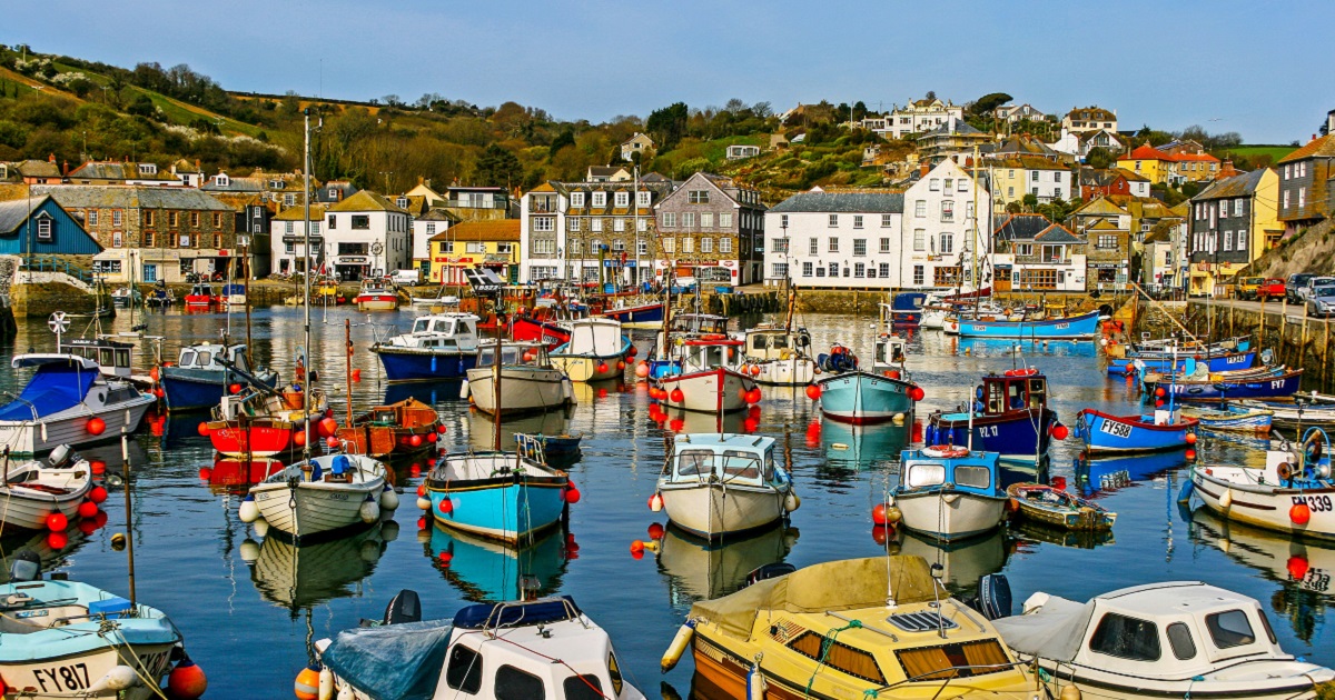 Image shows a picturesque harbour in Cornwall with lots of colourful boats and quaint houses on the bay