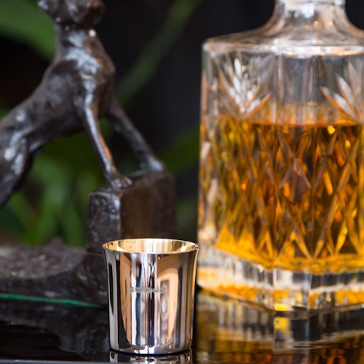 Large glass bottle of whiskey and a small sterling silver whiskey cup