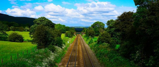 Image shows train tracks from the viewpoint of the train, heading into beautiful countryside