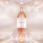 A light pink bottle of Gusbourne English Rosé in clear glass with matching top and a crystal bottom, set against a pink background