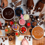 A table with lots of people reaching for melted chocolate, sweets and other ingredients in the centre of the table.