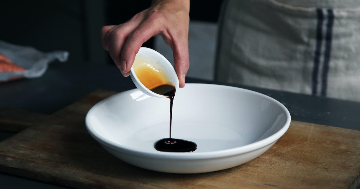 Small white bowl with soy sauce being poured into large white bowl
