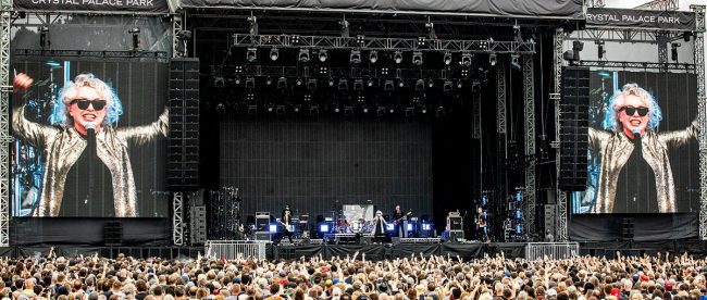 Image shows a wide angle shot of an outdoor music stage with Blondie performing