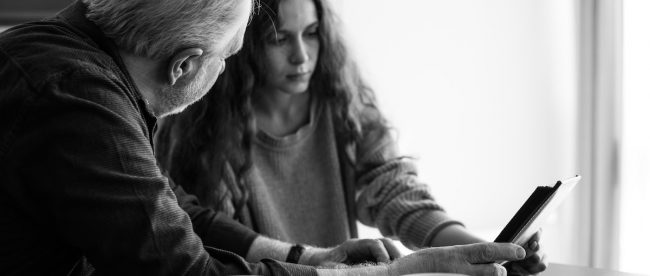 An older man and a younger woman looking at a photo album together. Picture in black and white.