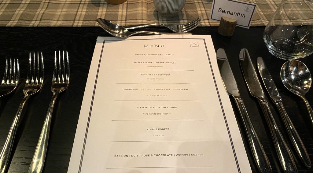 Image shows a menu and dinner setting with knives and forks. 