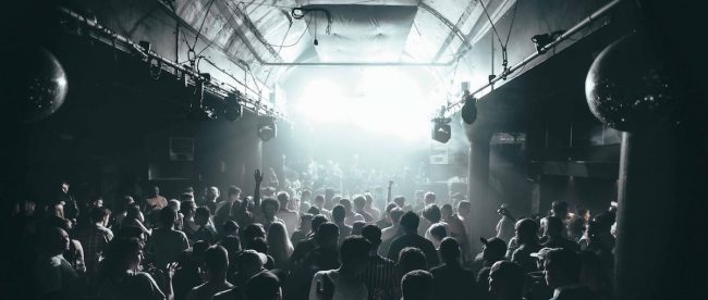 A crowd on people in a darkened club with white light emanating from a stage. noisenight venue for classical club night in Brighton.