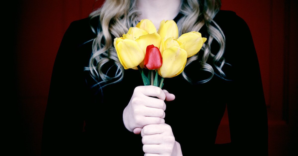A woman dressed in black holding a bunch of yellow tulips with one red tulip close to the camera. Funeral crasher confessions on Silver.