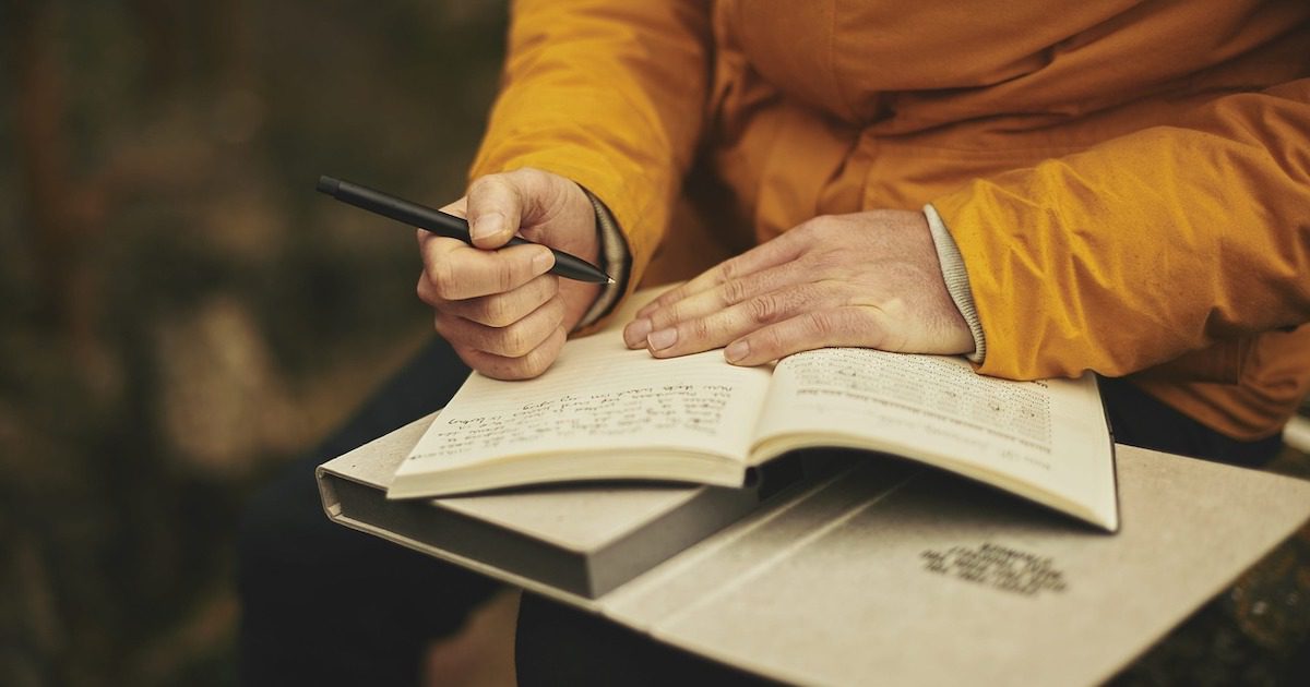 Someone in a yellow raincoat, writing in a journal.