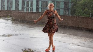 Image shows a woman dancing around on her own in the summer rain