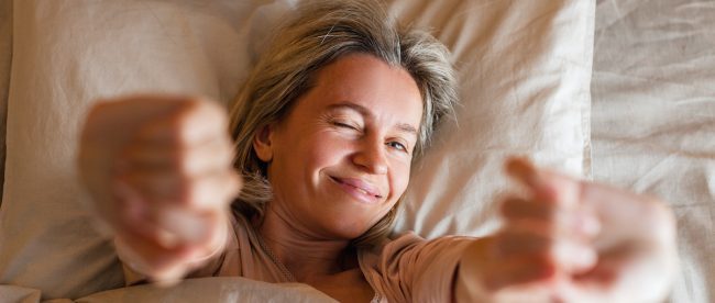 Woman lying in bed stretching in the morning. How to get to sleep and which hacks to avoid.