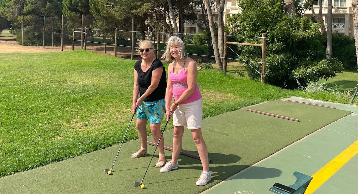 Two mature friends at a driving range with gold clubs posed. Taking a holiday alone and making friends