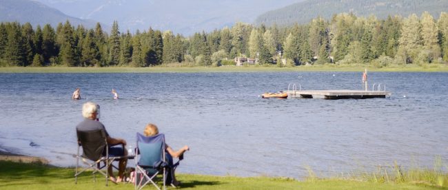 Mature couple sat in camping chairs looking out at river with trees in the distance. Holidays for retirees on Silver
