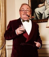 Gentleman dress in costume of red velvet blazer, bow tie, glasses, and a pipe. Theatre over 50 profile of Tim Ingram