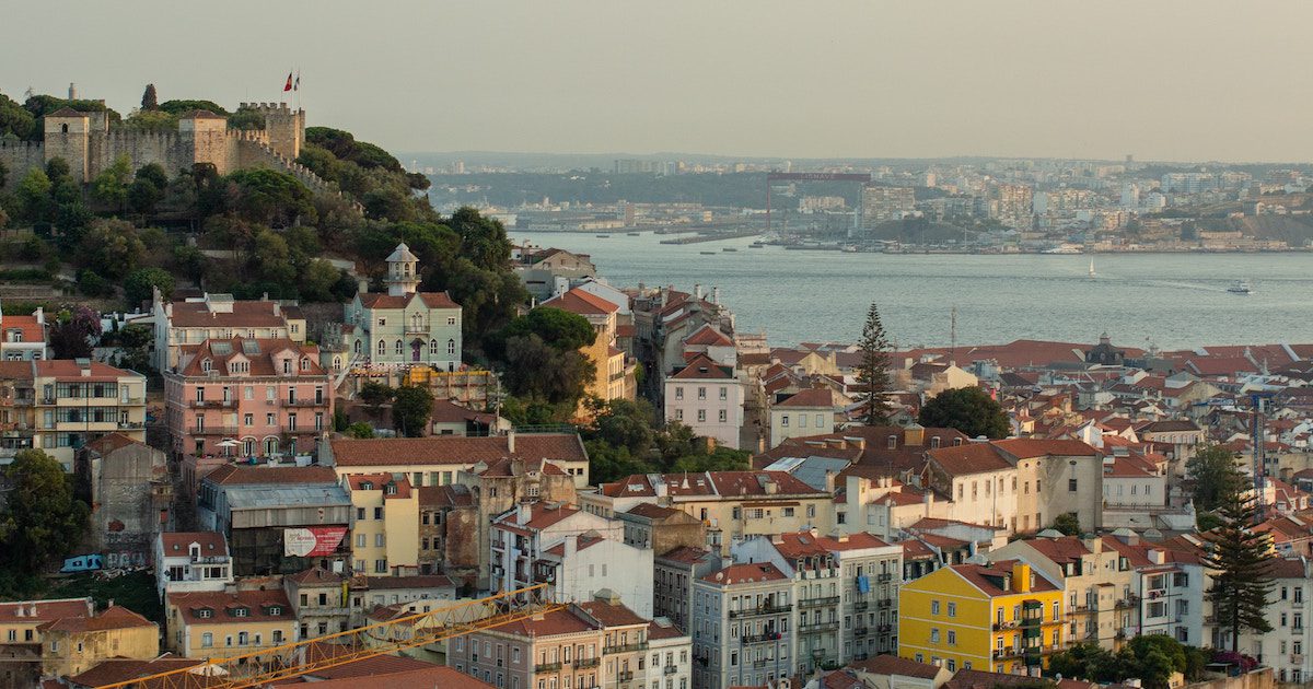 City skyline of red roofed building in Lisbon with water in the distance. September city break ideas