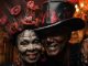 Two people smiling with large, extravagant, red and black hats and black face paint as Halloween costumes