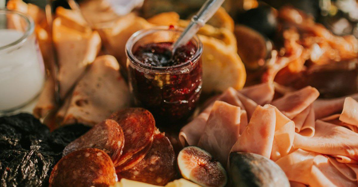 A jar of chutney nestled between a platter of meats, figs and other charcuterie