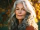 Smiling middle age grey-haired woman. Autumn leaves behind her