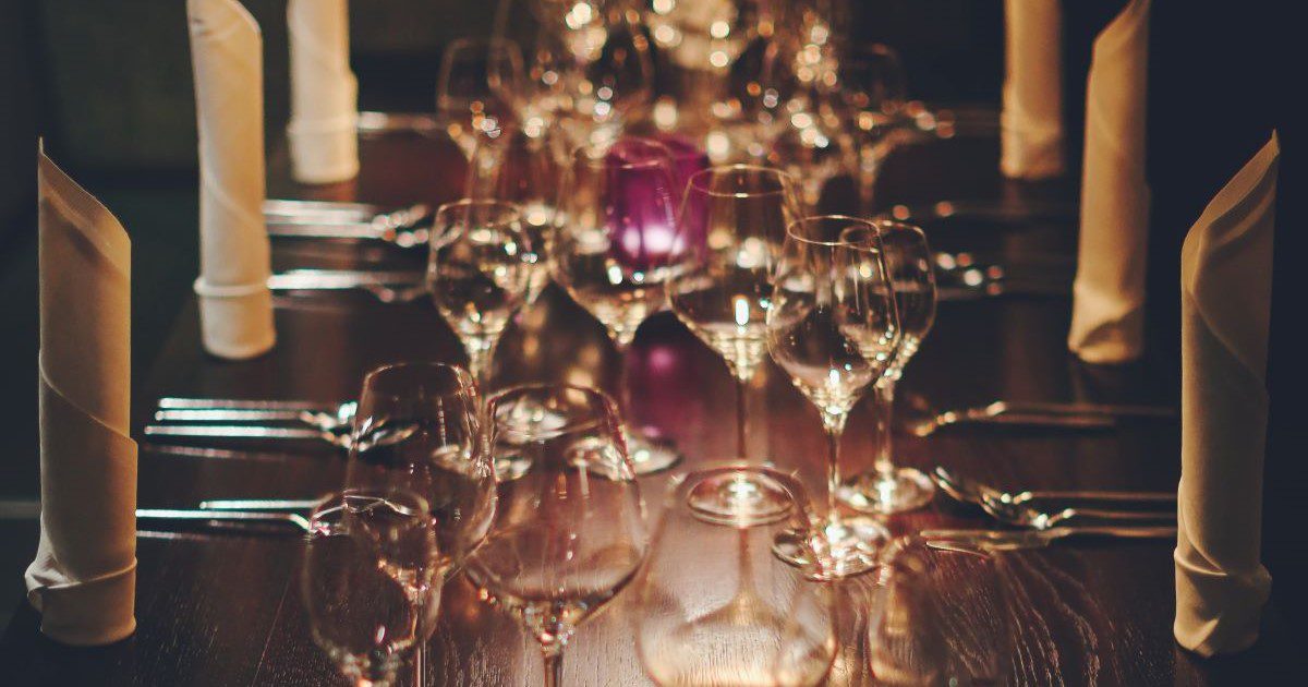 A long table lined with wine glasses and tall candles. The table is dimly lit