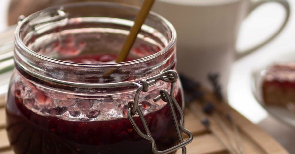 A close up of an open jar of jam with a stirrer inside