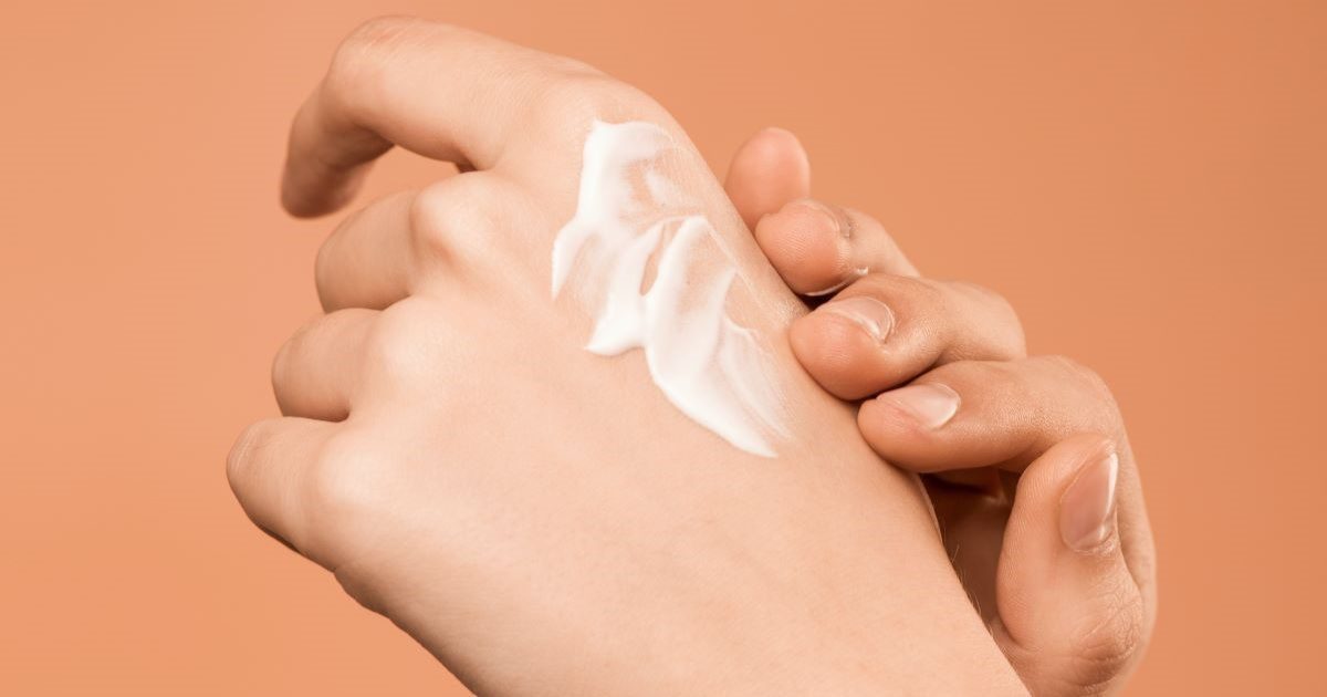 Hand rubbing cream into the other hand on a plain background