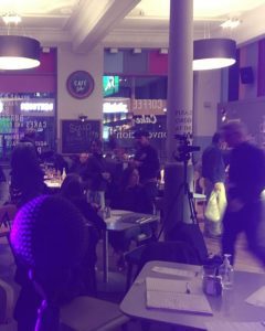 View from the stage of Cafe Sobar, a no alcohol bar. A microphone is in the foreground with the background showing a number of patrons sat around tables in a blue-lit space.