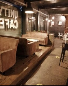 Inside of George Street Social, a no alcohol bar. Simple brown sofas facing each other beside a wall with a backwards sign that reads "UNITY CAFE". The sofas are on a platform with other tables visible to the right.