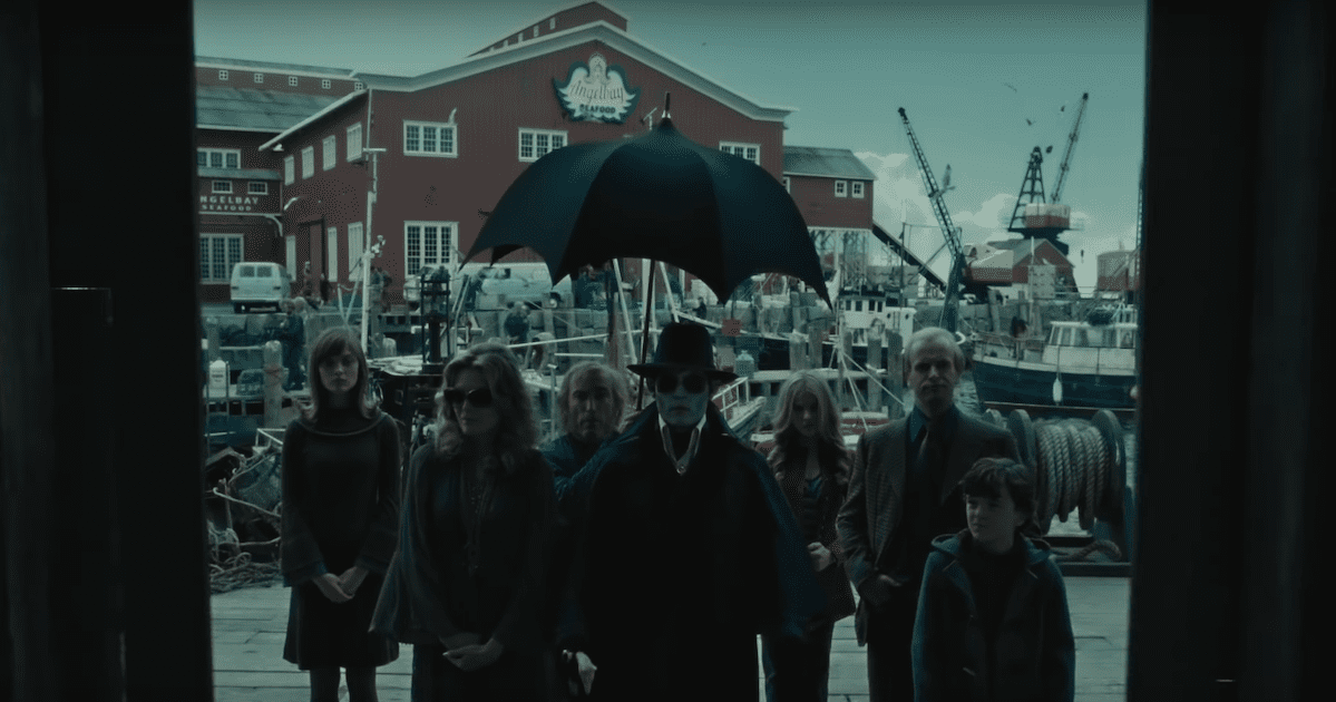 Man in suit and hat stands under an umbrella with a group of 70s dressed people stood behind him to his left and right from Dark Shadows. Halloween films not scary.