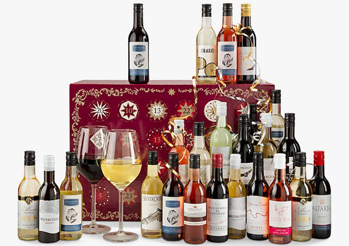 Advent calendar in red burgundy calendar with small wine bottles surrounding it and two glasses of wine, one reed wine and one white wine, stood next to the calender.