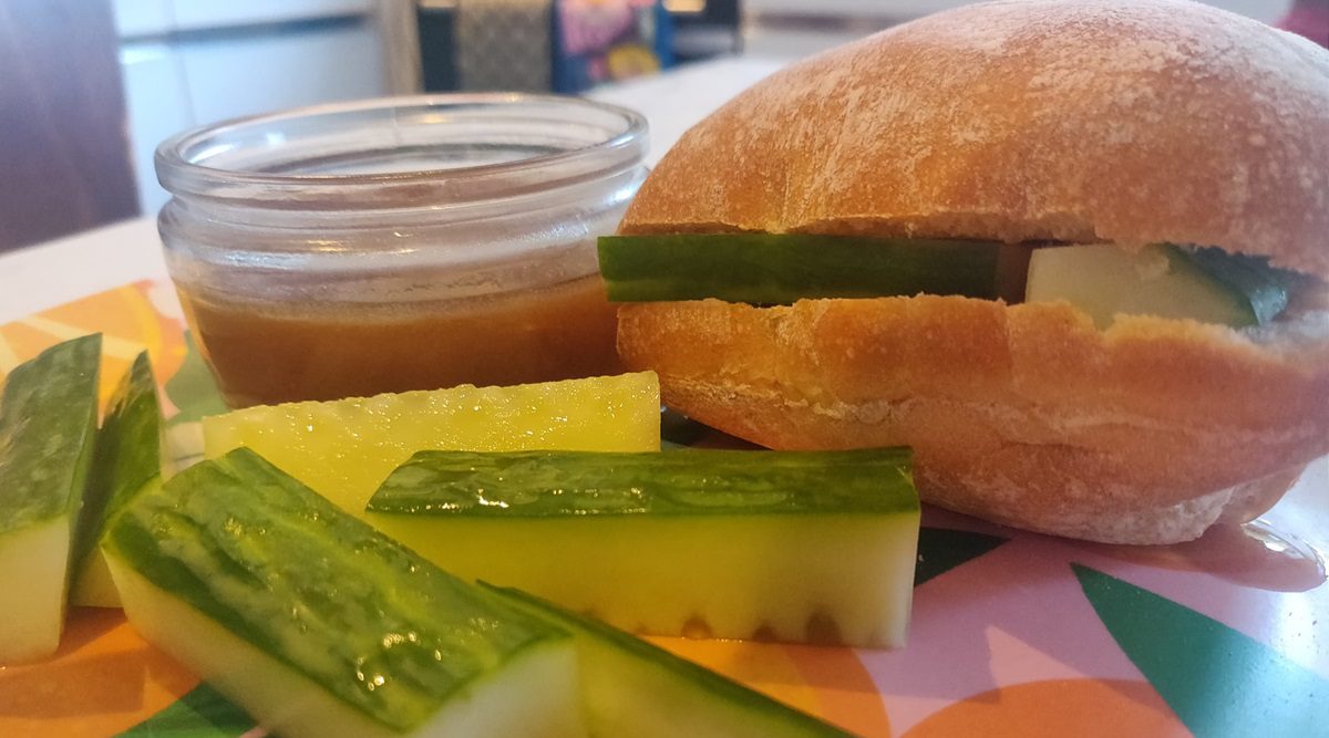 Plate showing all the ingredients for the sandwich, including a pot of gravy, cucumber sticks and a roll