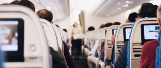 Image of the aisle of an aeroplane, with people seated and a blurred person walking down the aisle.