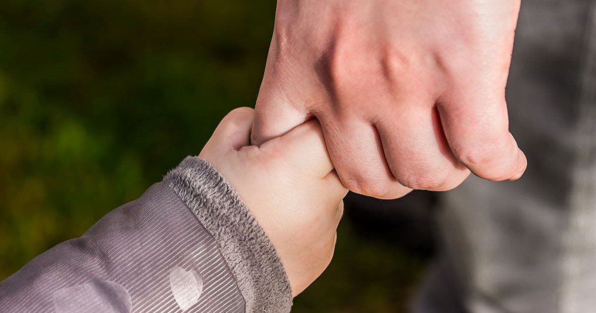 Image of a baby's hand holding the little finger of an adult's hand.