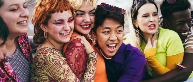 Image of a group of young queer people hugging each other with huge smiles.