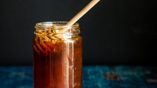 Image shows black background, jar of honey with a dropper dipped into the top of the honey