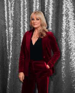 Tamzin Outhwaite stands in red velvet suit and black blouse against a glittery backdrop. Women's party wear