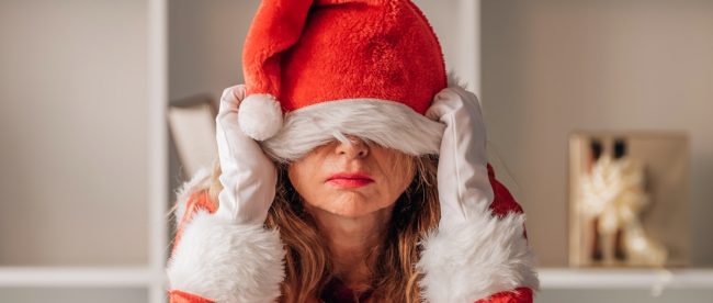 image shows a fed up woman pulling a santa hat down over her face, had enough of Christmas