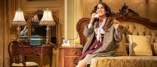 Image shows Sarah Jessica Parker on stage in character, sitting on a bed, using the old fashioned phone