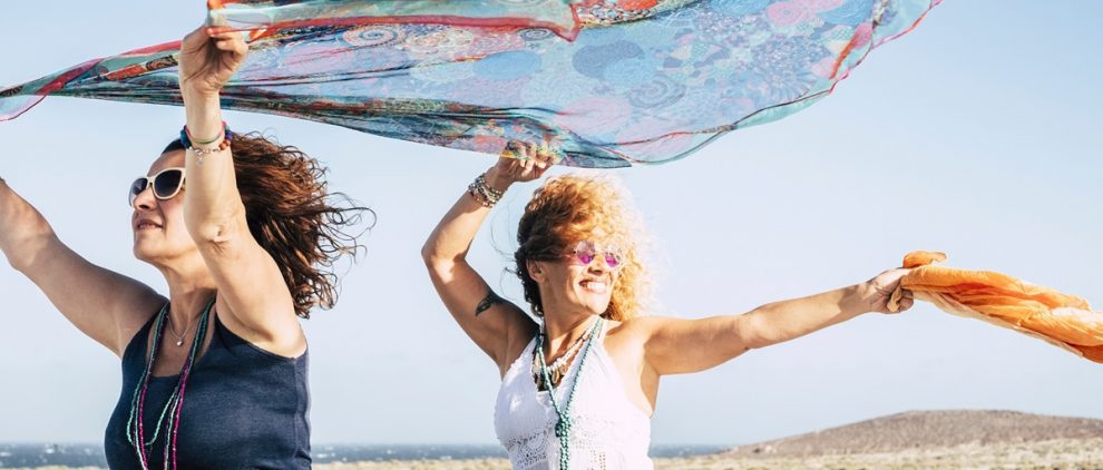 Couple of women have fun and play with the wind standing out of the top of a convertible car and playing with coloured pareos - cheerful people traveling and enjoying the outdoor on vacation