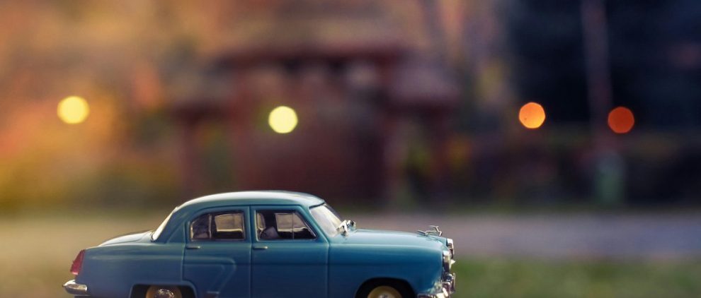 small blue toy car in front of a building and some grass