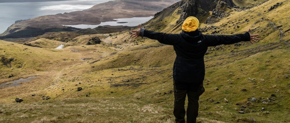 WOman with hands up stood in front of idyllic mountains and sea on her own